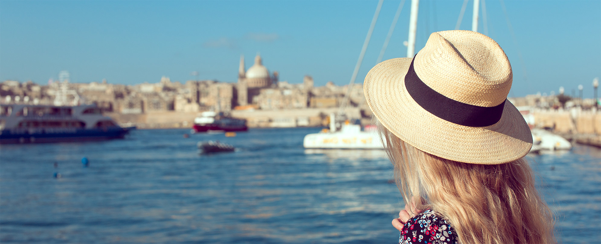 A woman wearing a hat looking over a city and water on a river cruise.