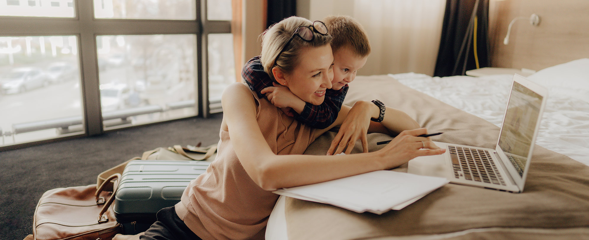 Little boy with his arms wrapped around his mother as she works on her laptop. 