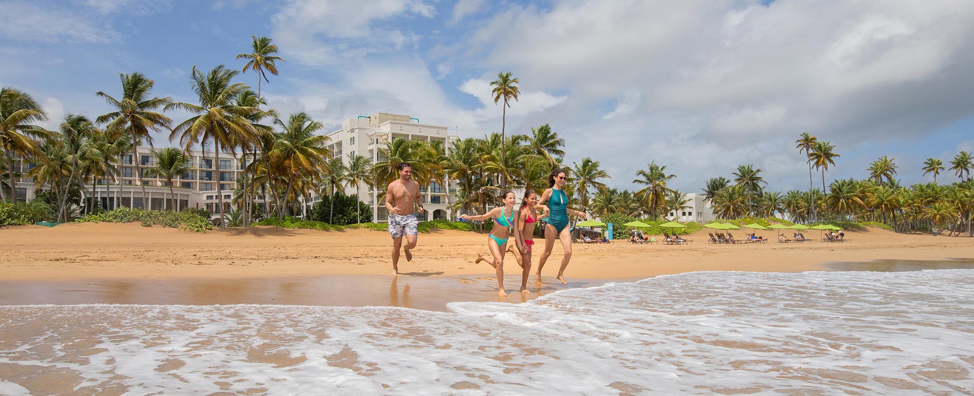 Mom, dad, and two young daughters running into the ocean on vacation at Margaritaville Vacation Club by Wyndham - Rio Mar.