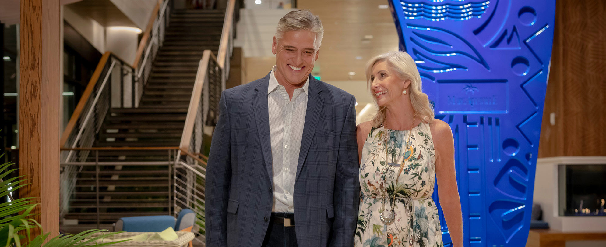 An older couple holding hands walking through a Margaritaville Vacation Club resort lobby. 