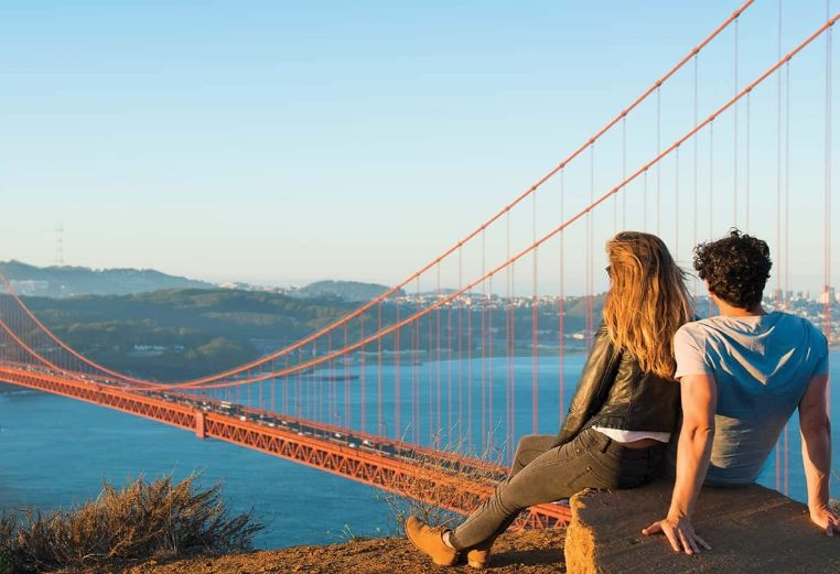 A couple sitting close together looking at an incredible view of the Golden Gate Bridge in San Francisco, CA. 