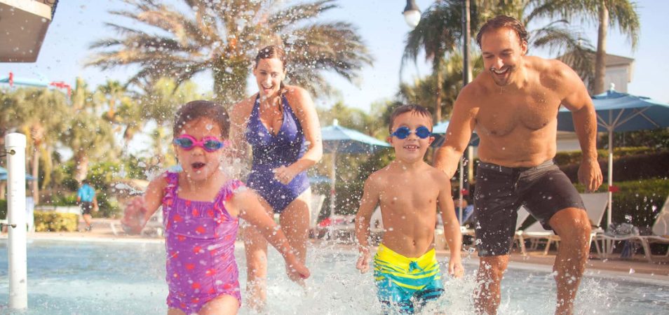 Parents with two young kids wearing goggles run through a splashpad at a timeshare resort.