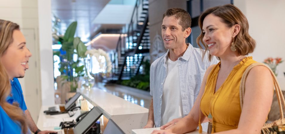 Man and woman standing at the check-in counter across from a female employee at a Margaritaville Vacation Club resort.