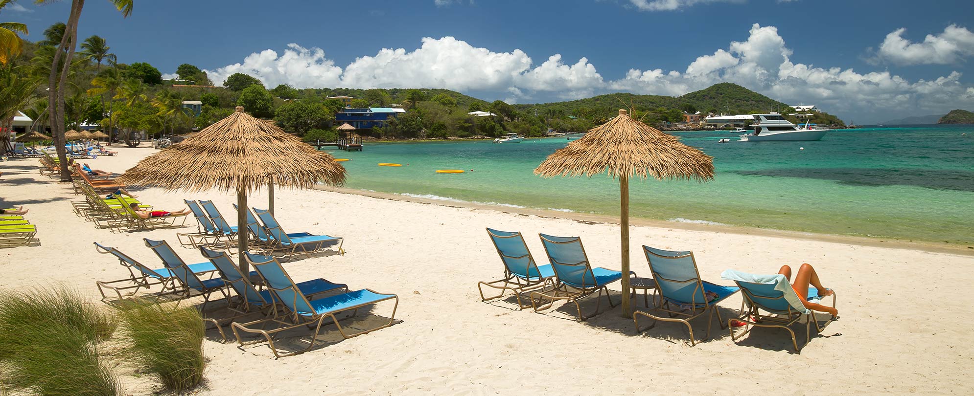 Guests lay by the ocean on beach chairs under straw umbrellas at Margaritaville Vacation Club by Wyndham - St. Thomas.