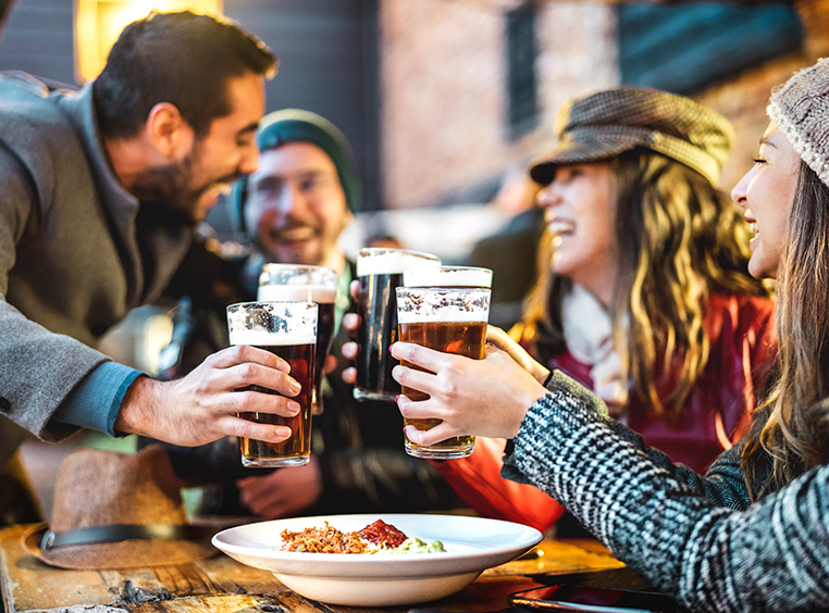 A group of friends wearing cold weather clothes share a toast by clinking their pints of beer.