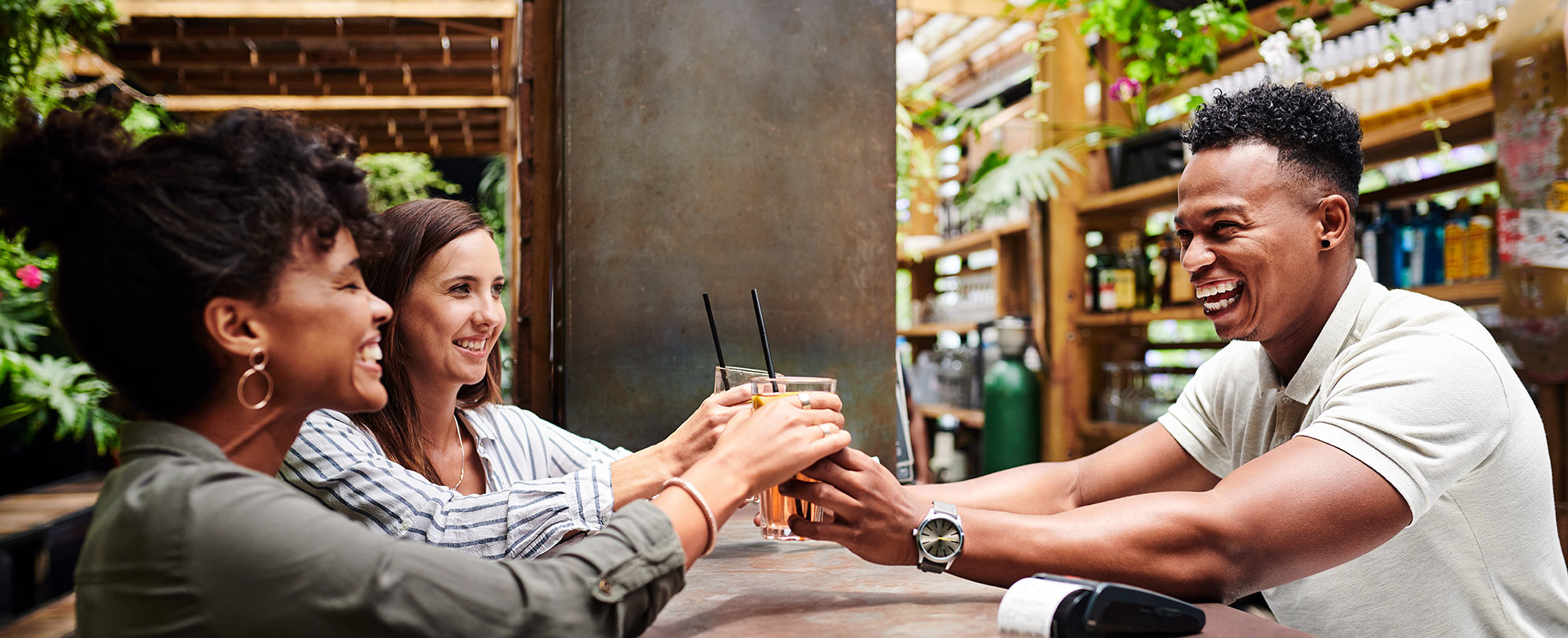 Smiling man serving two women drinks over a bar.