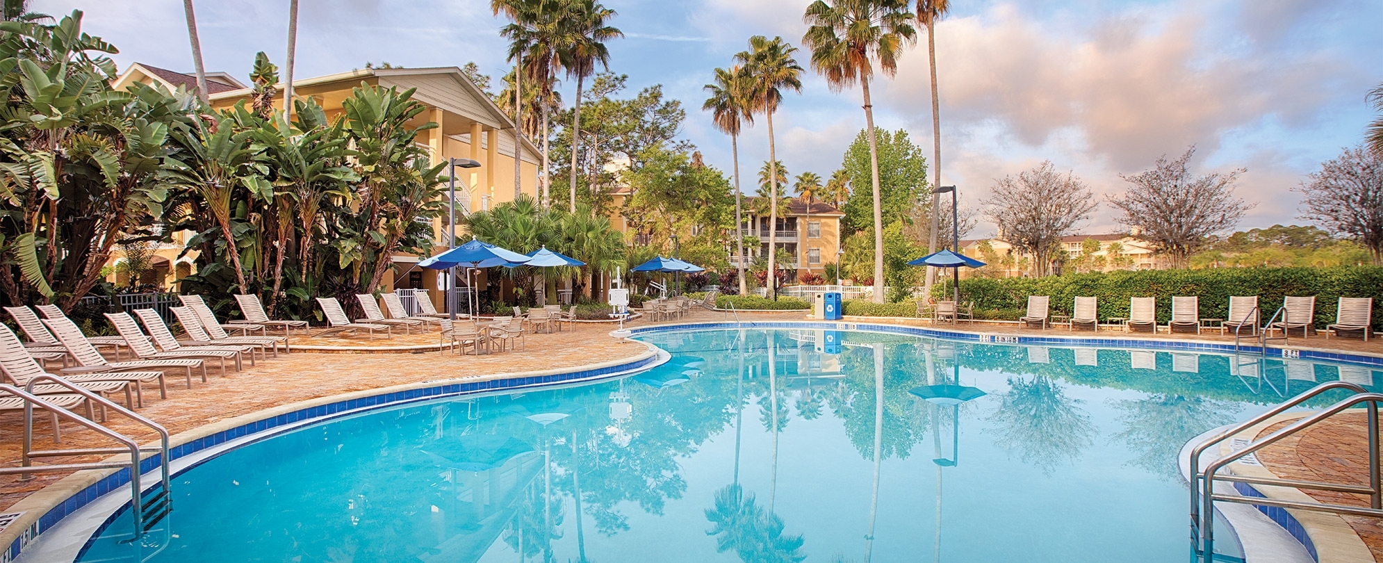 Outdoor resort pool surrounded by pool chairs and palm trees at Club Wyndham Cypress Palms, a timeshare resort in Kissimmee, FL.