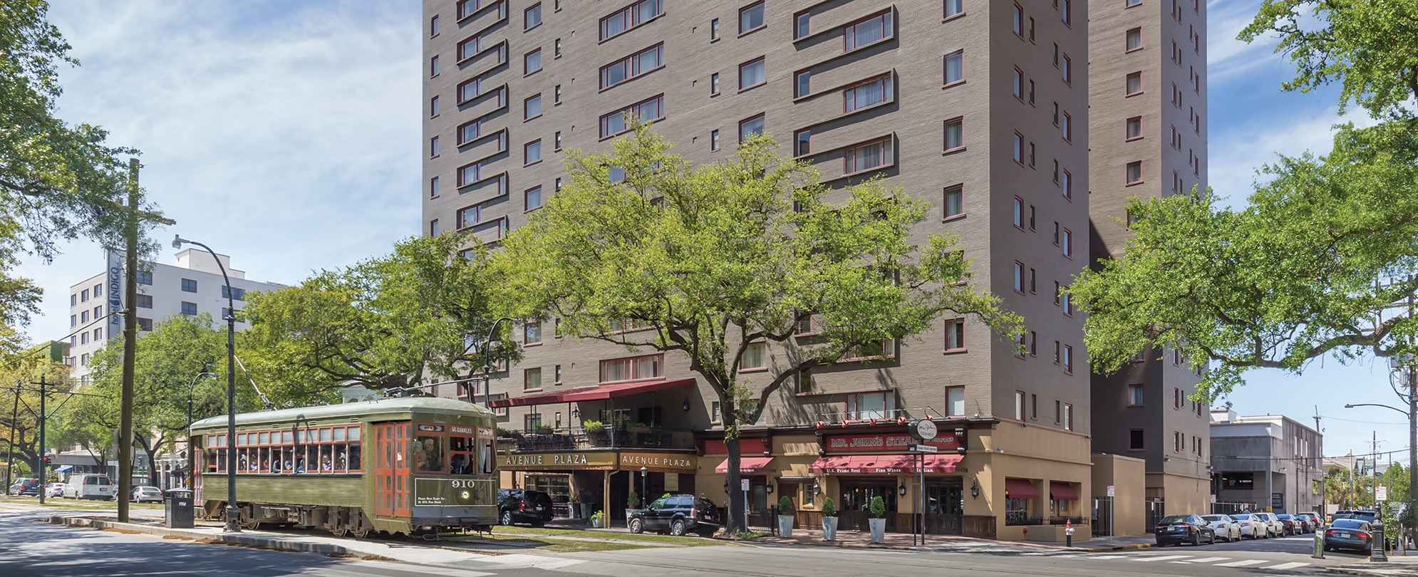 The exterior of the Avenue Plaza timeshare resort in New Orleans, Louisiana with a trolly car in front. 